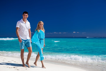 Fototapeta na wymiar Happy couple walking on beach, smiling and looking at camera