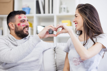 Man and woman connected with his fists in the form of heart. Small DOF, focus on hands. Man with kisses marks on his face.