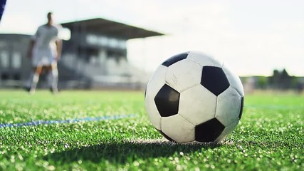 Close up of a soccer ball being kicked by a player in slow motion, with players in the background