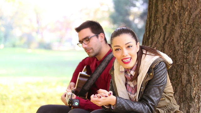 Woman singing and man playing guitar while sitting on a tree in park