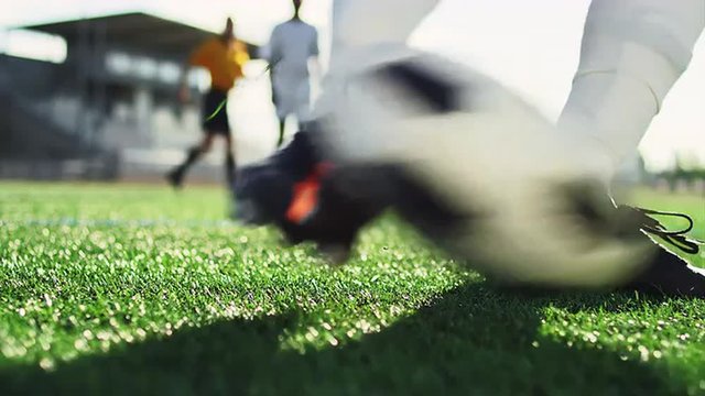 Close up of a soccer ball being kicked by a player in slow motion, with players in the background