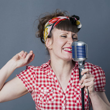 fifties singer in studio - fun young female rocker with retro style snapping her fingers for rhythm, singing in old fashioned micro, gray background....