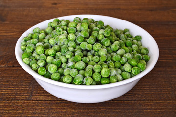 Bowl of frozen peas on wooden table