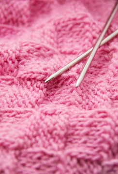 Detail of woven handicraft knit woolen design texture and knitting needle. Fabric pink background