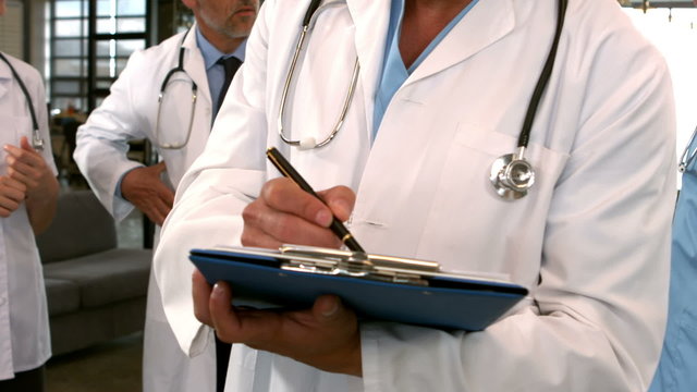 Mid section view of doctor writing on clipboard