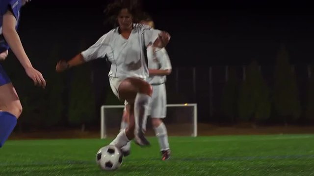 A female soccer player dribbles down the field during a game at night