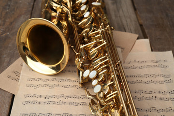 Obraz premium Beautiful golden saxophone with musical notes on wooden background, close up