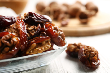 Walnut and date fruit in plate on wooden table, close-up