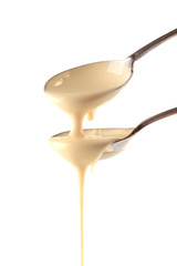 Condensed milk pouring from spoons, isolated on white