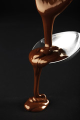 Chocolate poured on a spoon on dark background