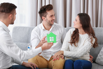 Estate agent with model of house and happy couple on home interior background