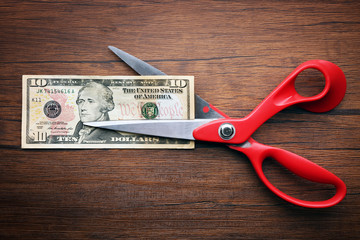 Red scissors cut money on wooden background. Financial concept