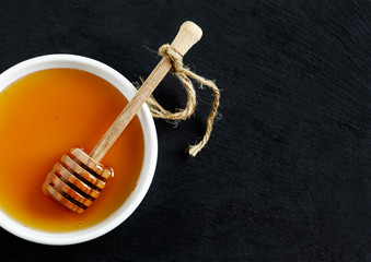 Honey and honey dipper on black background