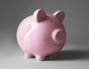 Piggy Bank with adhesive bandage on grey background
