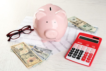 Bookkeeping concept. Piggy bank, calculator, dollars and papers on white wooden background