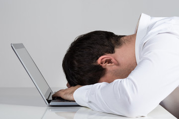 Stressed Businessman Leaning On Laptop At Desk