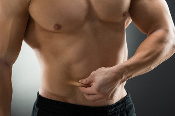 Obraz premium Midsection Of Muscular Man Holding Fat Belly