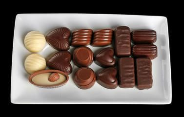 Assorted chocolate candies on white plate over black background