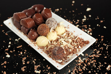 Assorted chocolate candies on white plate with flakes over black background