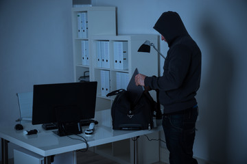 Burglar Putting Laptop Into Bag At Desk In Office