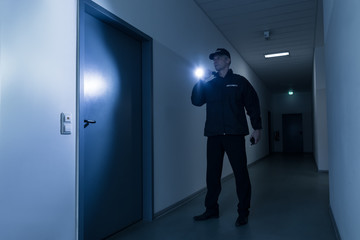 Security Guard With Flashlight Standing In Front Of Door - obrazy, fototapety, plakaty