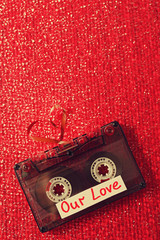 Retro audio cassette with tape in shape of heart on red textured background