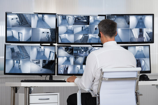 Security System Operator Looking At CCTV Footage At Desk
