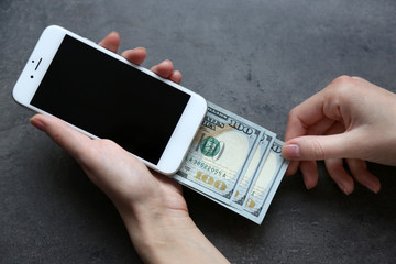 Hands holding smart phone with dollar banknotes on grey background. Making money online