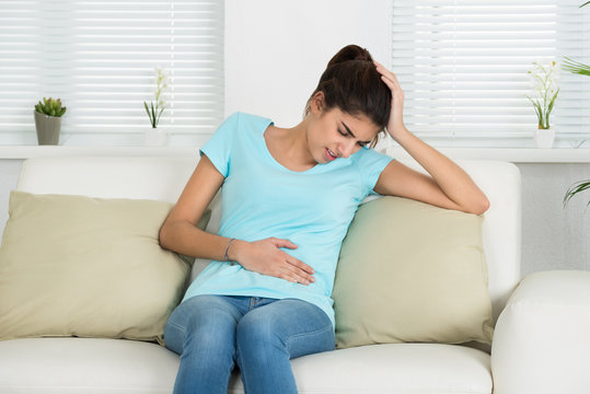 Woman Suffering From Stomach Ache Sitting On Sofa