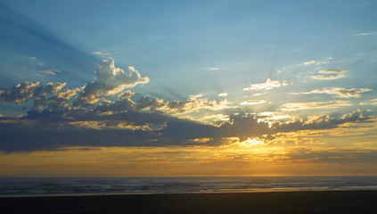 Obraz premium Cloudy Sunset Over the Ocean with Sunbeams in the Sky