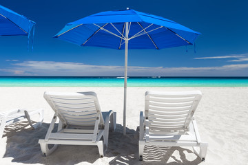 Caribbean beach with blue sun umbrellas and white beds