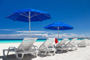 Fototapeta na wymiar Caribbean beach with blue sun umbrellas and white sunbeds