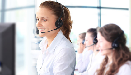 Smiling female customer service representative talking on headset with colleagues in background at...
