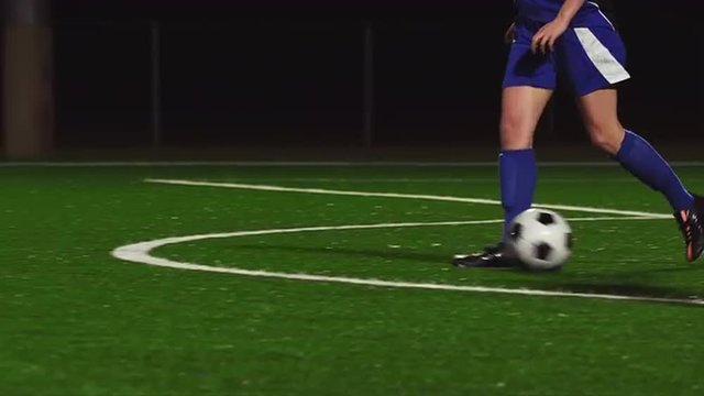 Female soccer players dribbling down the field during a game at night