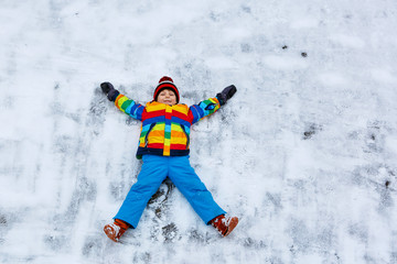 Fototapeta na wymiar Little kid boy making snow angel in winter, outdoors