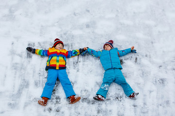 Two little kid boys making snow angel in winter, outdoors