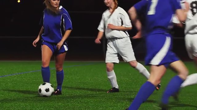 Female soccer players pass the ball during a game at night and make a goal
