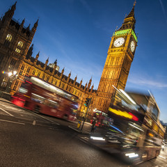 a fuzzy moving doubledecker bus passes lit big ben and parliament in the evening