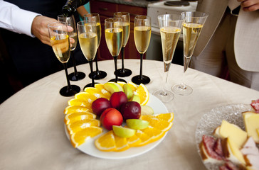 Дольки апельсинов, яблок и нектарины на блюде и бокалы с шампанским на круглом столе с белой скатертью