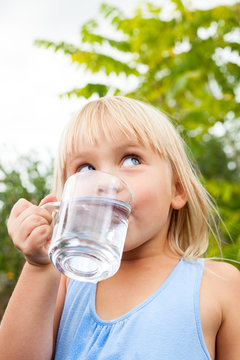 Little girl drinking water looking side in a summer garden