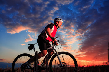 Naklejka premium Man Cyclist with bike on sunset