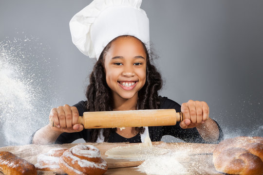 Little Dark-skinned Girl Rolls The Dough. The Child Learns To Cook. Clothing And Chef Hat