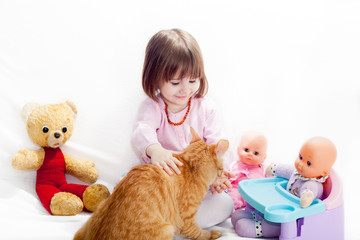 Little girl playing with toys and feeding a cat