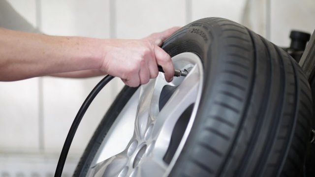 Car mechanic filling tire on alloy wheel with air