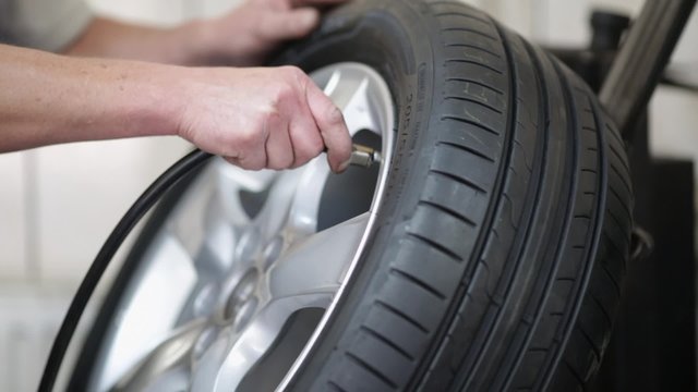 Closeup of car mechanic pumping tire with alloy wheel at auto service