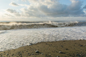 huge waves washing the gravel beach on the shore of the evening sea during sunset