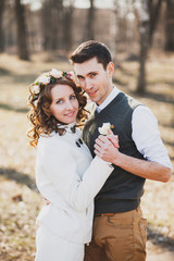 Young couple in love holding hands and looking at camera. Portrait of smiling woman and man on their wedding day. Spring or autumn wedding. People posing at bare trees background in forest or park.