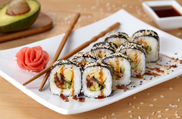Futomaki sushi roll with eel, cucumber, sesame seeds, ginger, and soy sauce.