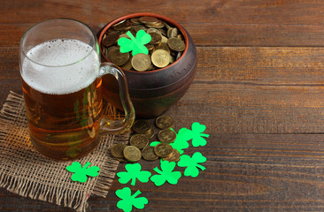 Fototapeta na wymiar Green Shamrocks clovers on wooden background with a large pot with a bunch of gold coins and a large mug of beer . Background for St. Patrick's Day celebration