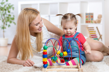 Kid girl plays with educational toy indoor. Happy mother looking at her smart daughter